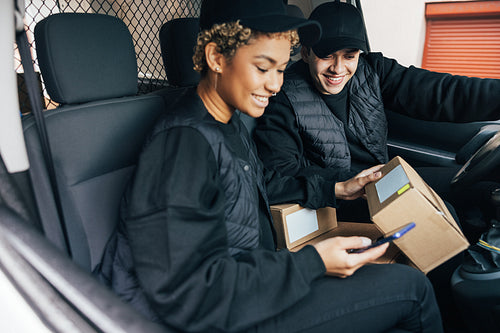 Two couriers sitting in car checking information on box using mo