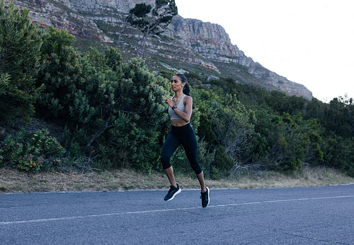 Full length of a young slim female practicing running outdoors on an abandoned road. Woman athlete jogging outdoors in natural park.