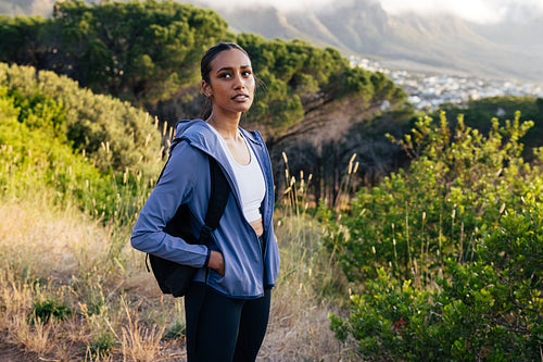 Confident sportswoman with backpack and sportswear standing in natural park