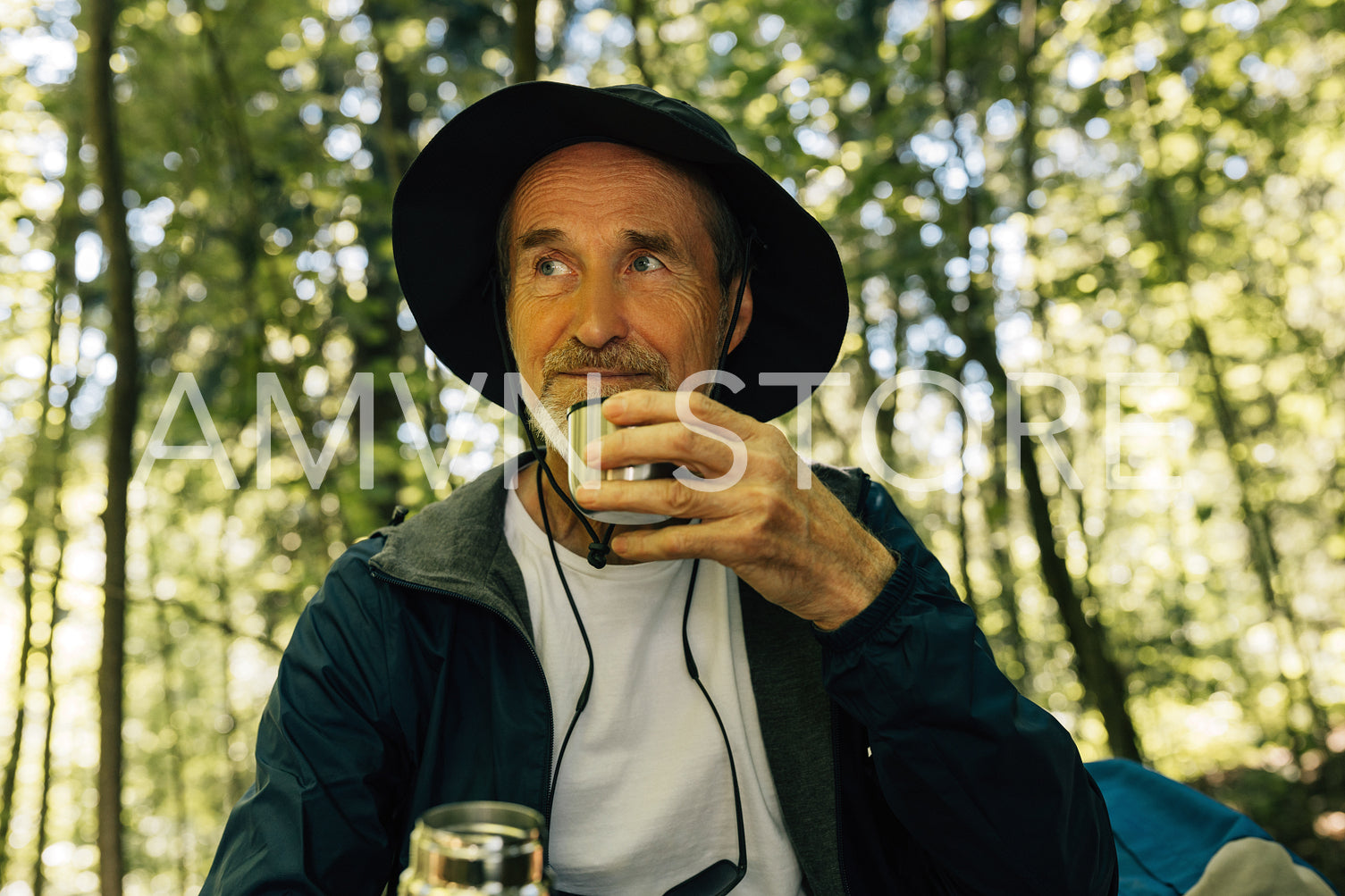 Male tourist in a hat drinks coffee from a cup. Senior tourist take a break during his forest tour.