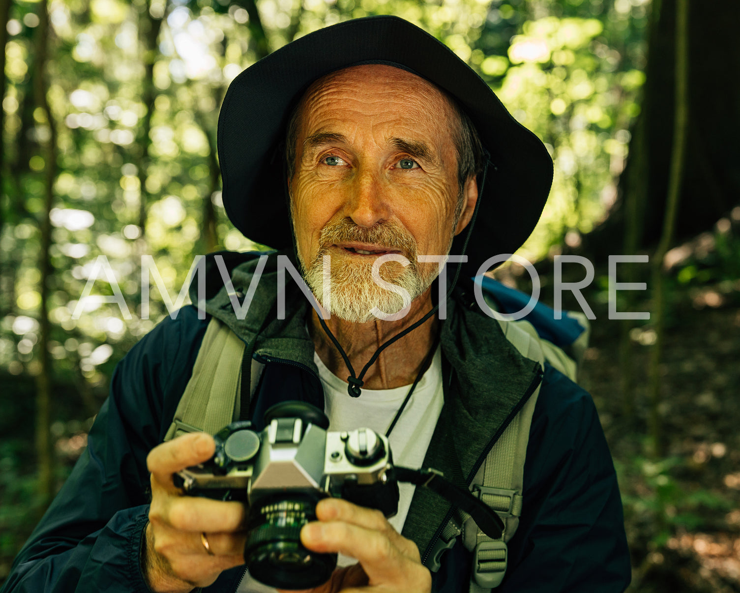 Close-up portrait of senior tourist with a film camera in a forest. Mature male with a retro camera during his hike.