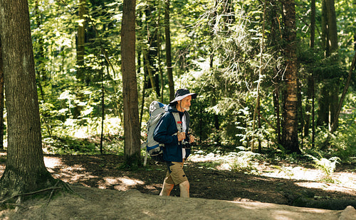 Side view of a senior male with a backpack and hiking clothes walking in the forest on sunny day