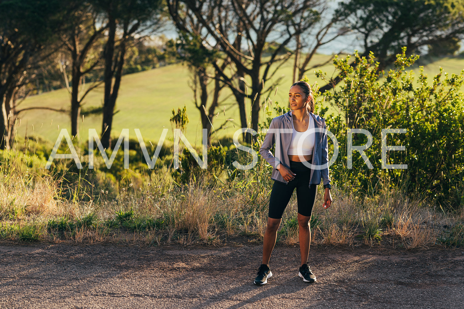 Full length of slim female in sportswear standing outdoors at sunset, taking a break