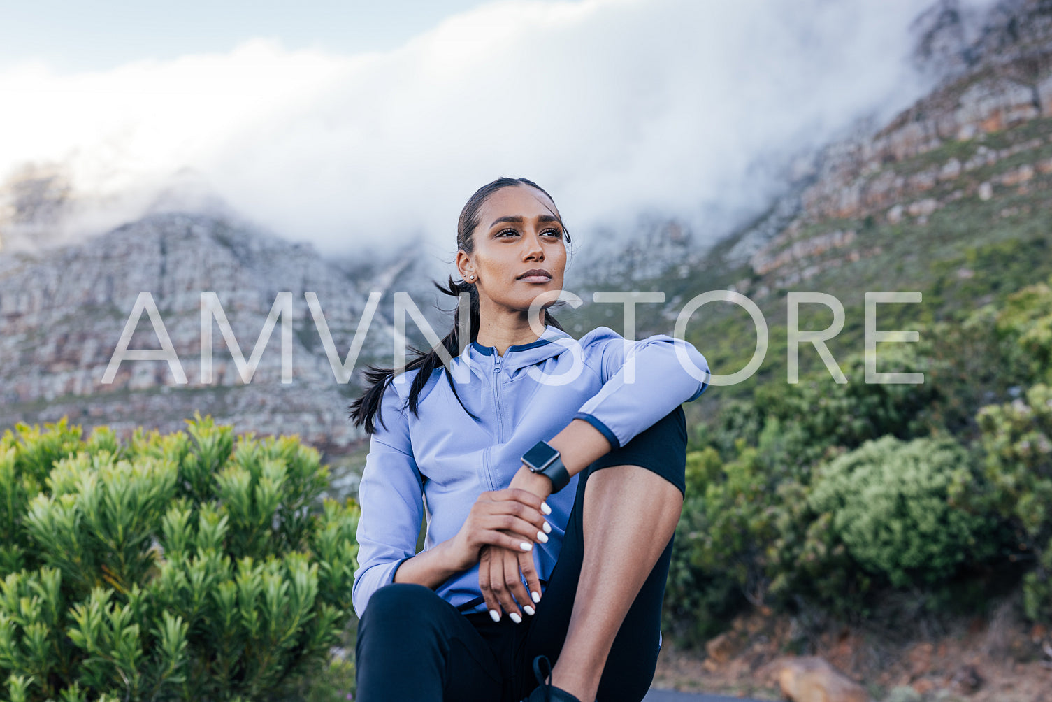 Confident slim female sitting against the stunning view in a natural park. Young woman in sportswear relaxing outdoors and looking away.