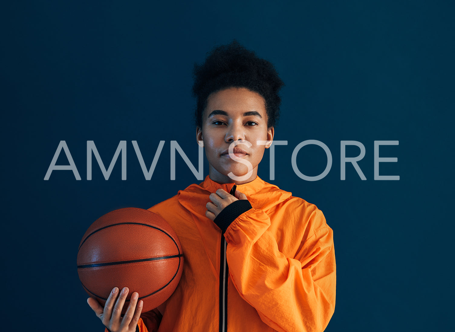 Young female adjusting her orange sportswear and looking at the camera over a blue backdrop. Professional female basketball player with the ball in the studio.