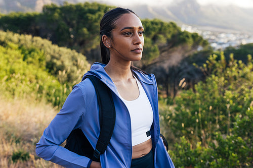 Portrait of young female in sportswear with backpack standing outdoors at sunset