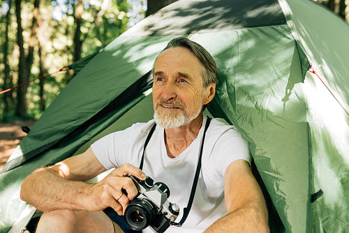 Male tourist with film camera sitting in forest. Senior tourist relaxing during his small adventure sitting near tent.