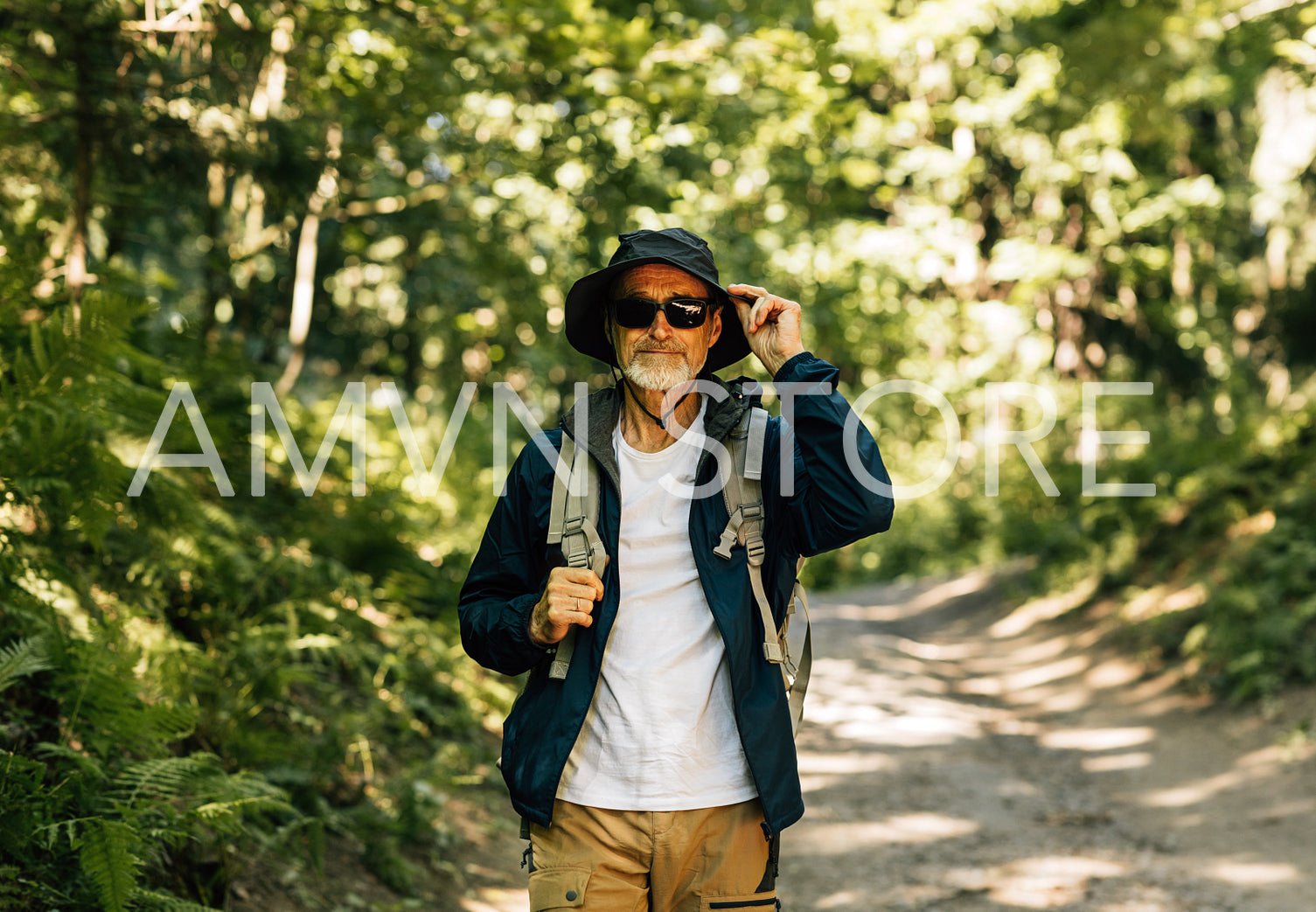 Senior male walking in the forest wearing eyeglasses and holding a hat. Mature man walking in the forest path.