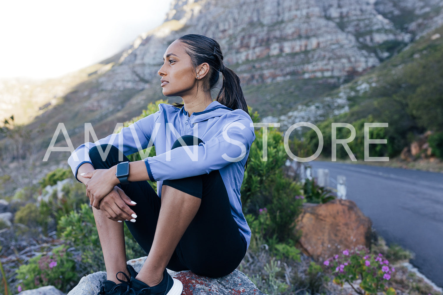 Young runner sitting outdoors on a rock in a natural park. Female in fitness attire enjoy the view while taking a break during outdoors workout.