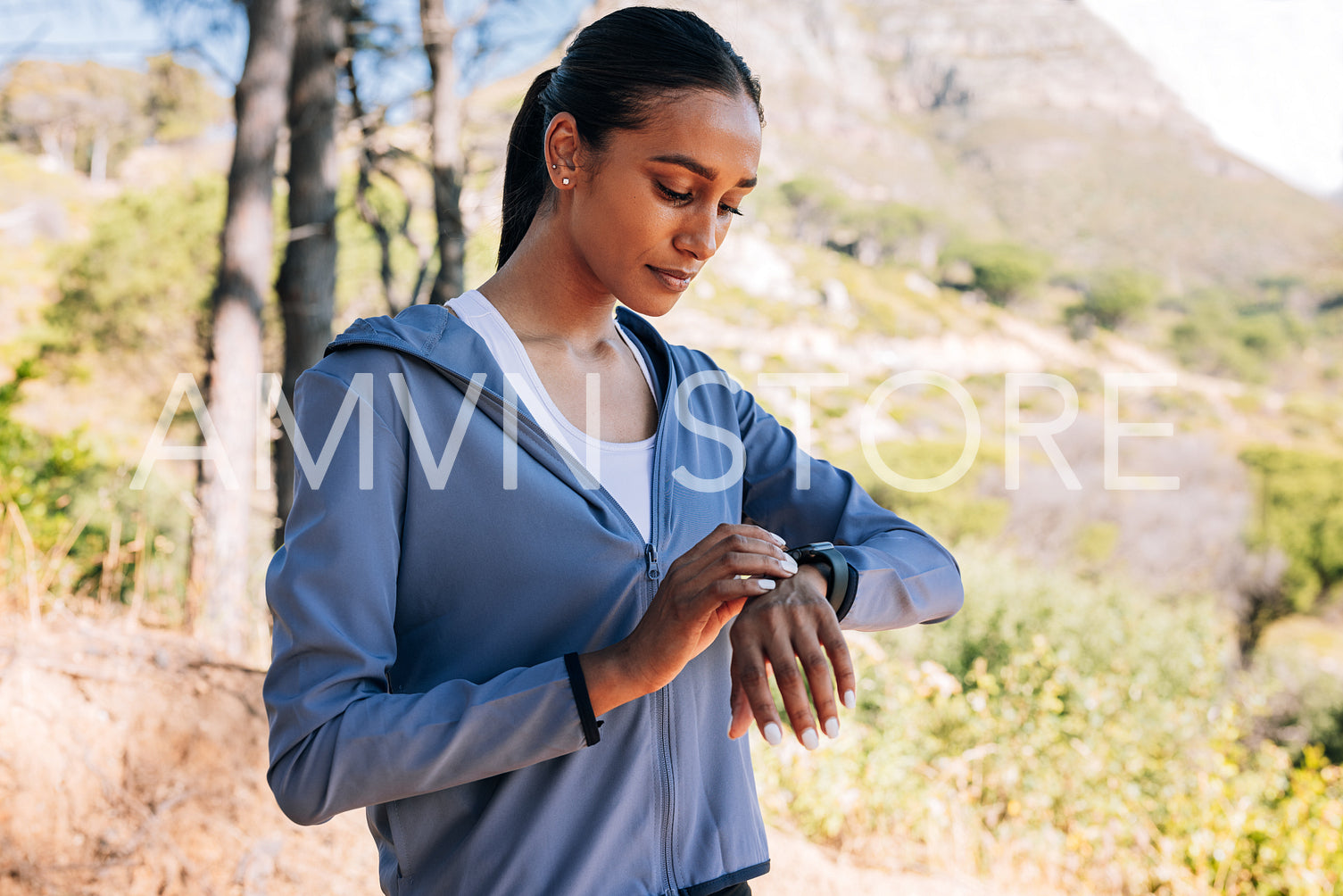 Young female checking her smartwatches during outdoor training. Slim woman in the park taking a break during a workout.