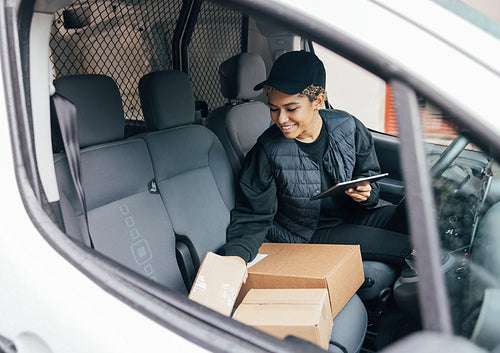 Smiling woman sitting on driver's seat checking packages and hol