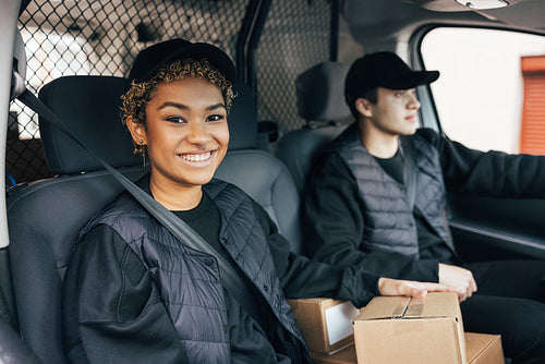 Smiling woman in uniform sitting in delivery van and looking at