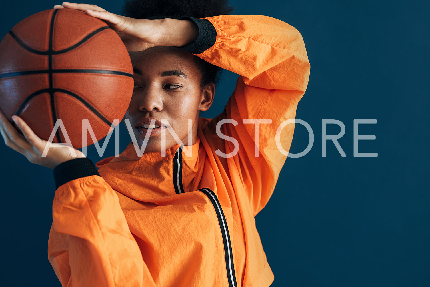 Close up studio shot of young female basketball player in orange sportswear posing with ball. Portrait of a professional basketball player over blue background.