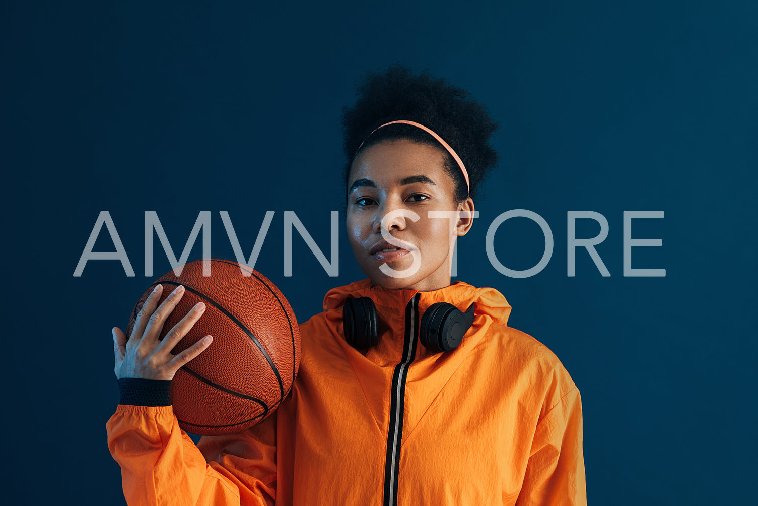 Portrait of confident female basketball player looking at camera in studio. Young woman with basketball posing over blue backdrop.