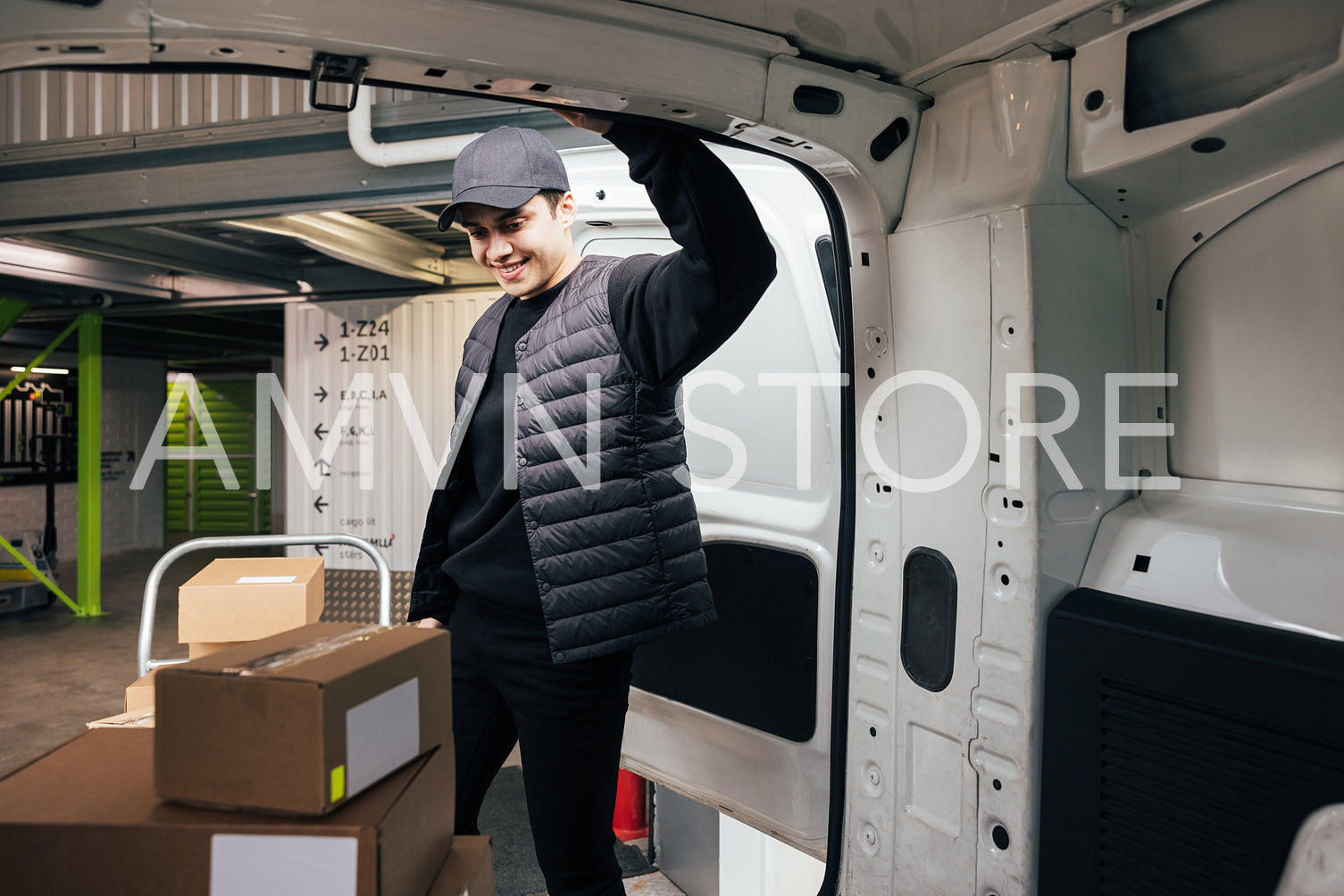 Confident courier leaning on van looking on cardboard boxes