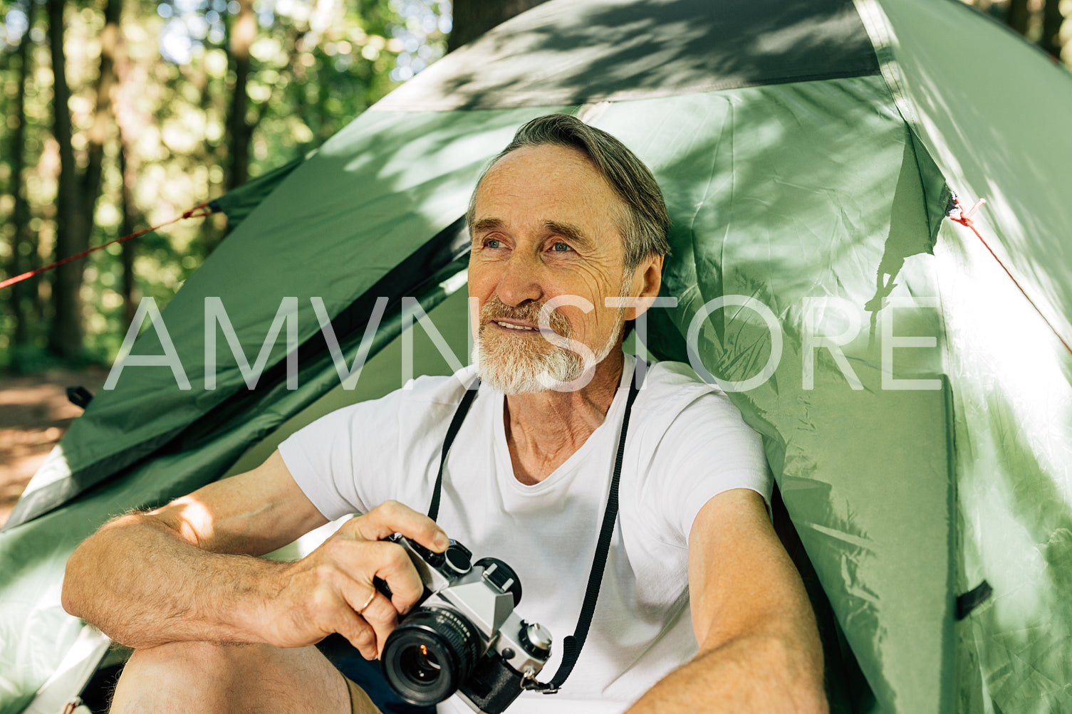 Male tourist with film camera sitting in forest. Senior tourist relaxing during his small adventure sitting near tent.