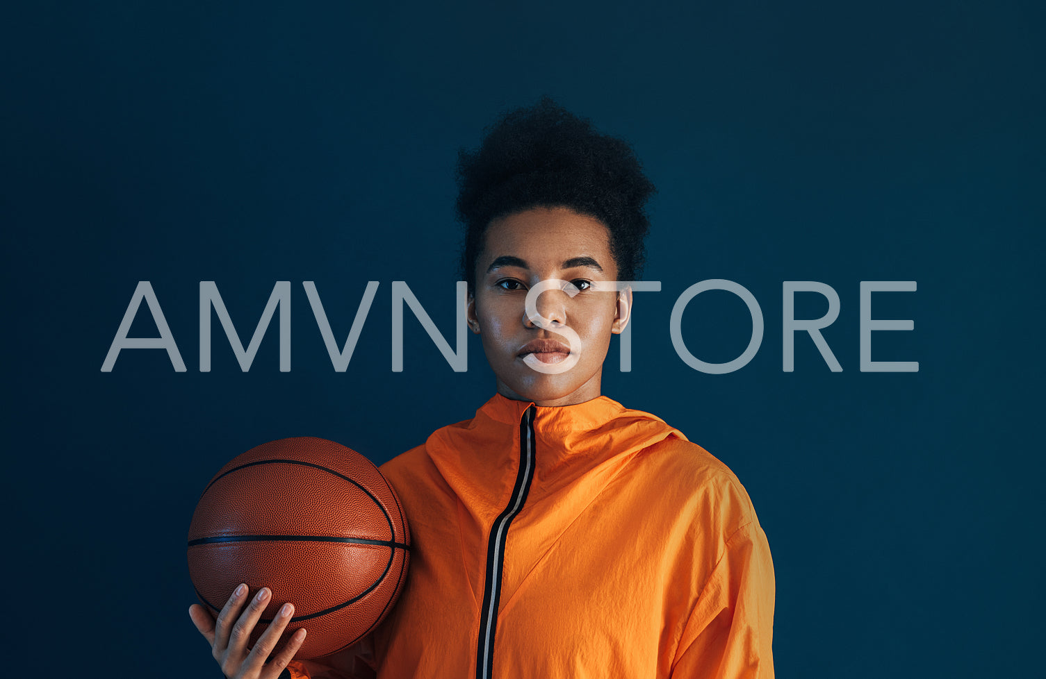 Portrait of young basketball player in orange sportswear posing in studio. Woman with a basketball standing against blue background.