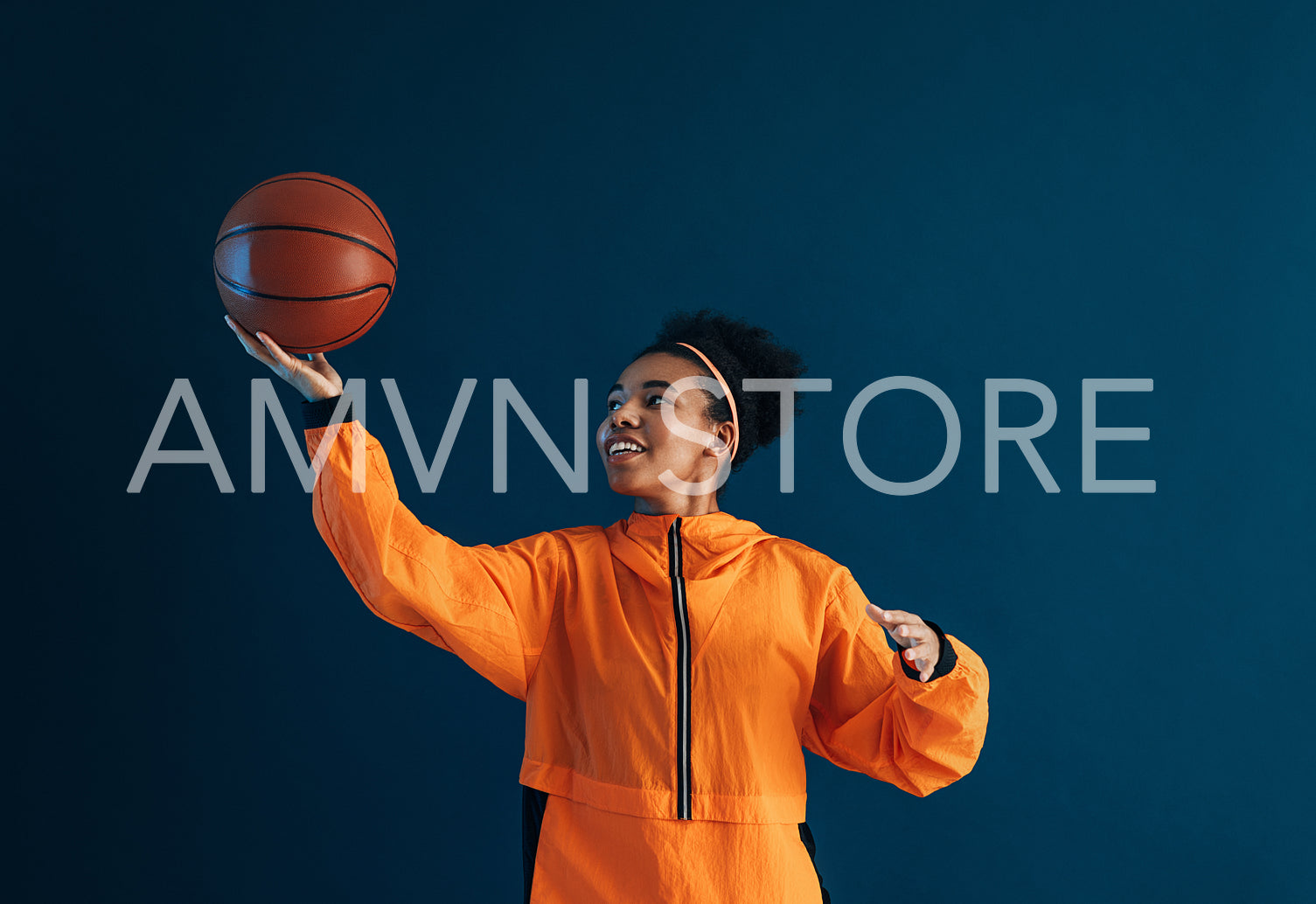 Young woman playing with a basketball in studio. Female in orange fitness wear with basketball practice moves.