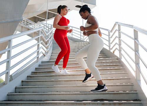 Two female friends running down on stairs. Women with different body types exercise outdoors together.