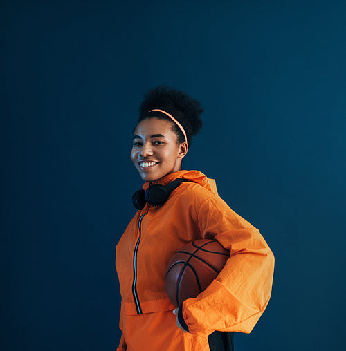 Professional basketball player in orange sportswear posing in studio against blue background