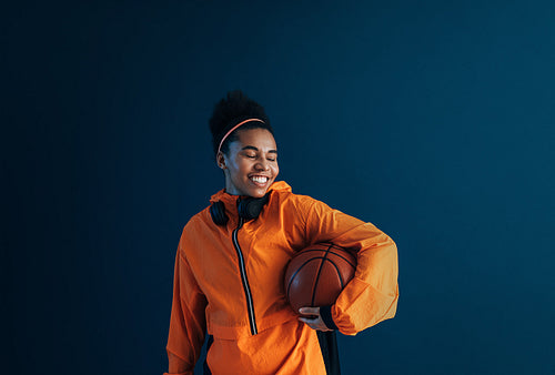 Young cheerful female with curly hair holding a basketball with eyes closed