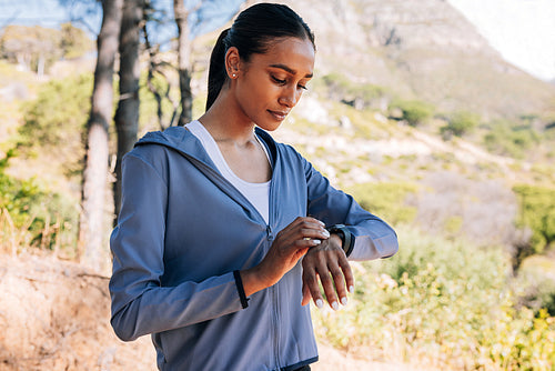 Young female checking her smartwatches during outdoor training. Slim woman in the park taking a break during a workout.