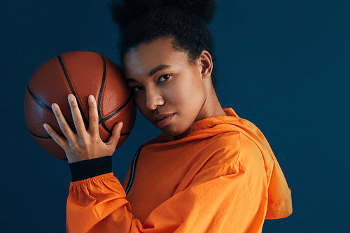 Portrait of a woman with a basketball against a blue backdrop. Studio shot of a confident female basketball player.