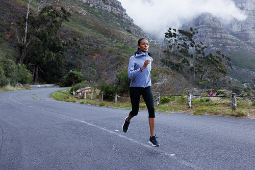 Full length of a slim female athlete running on an abandoned road. Woman in fitness attire jogging on the road in the mountains.