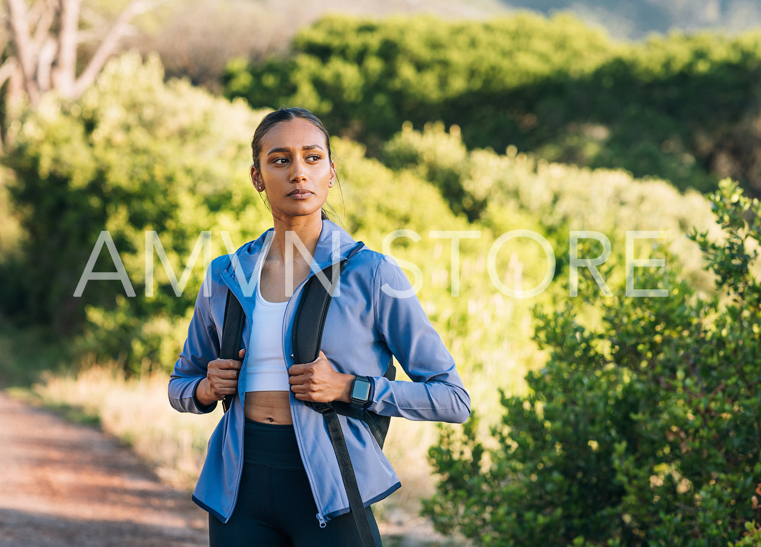 Portrait of a female hiker at sunset. Woman with a backpack wearing sportswear standing outdoors.