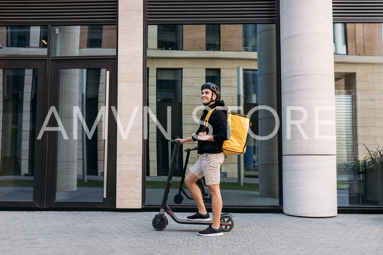 Smiling messneger man standing outdoors with electric push scooter. Delivery man with termal backpack in the city.