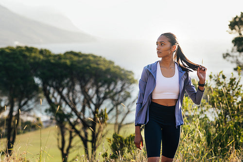 Slim female in fitness attire adjusting her hair while standing in front of stunning view at sunset