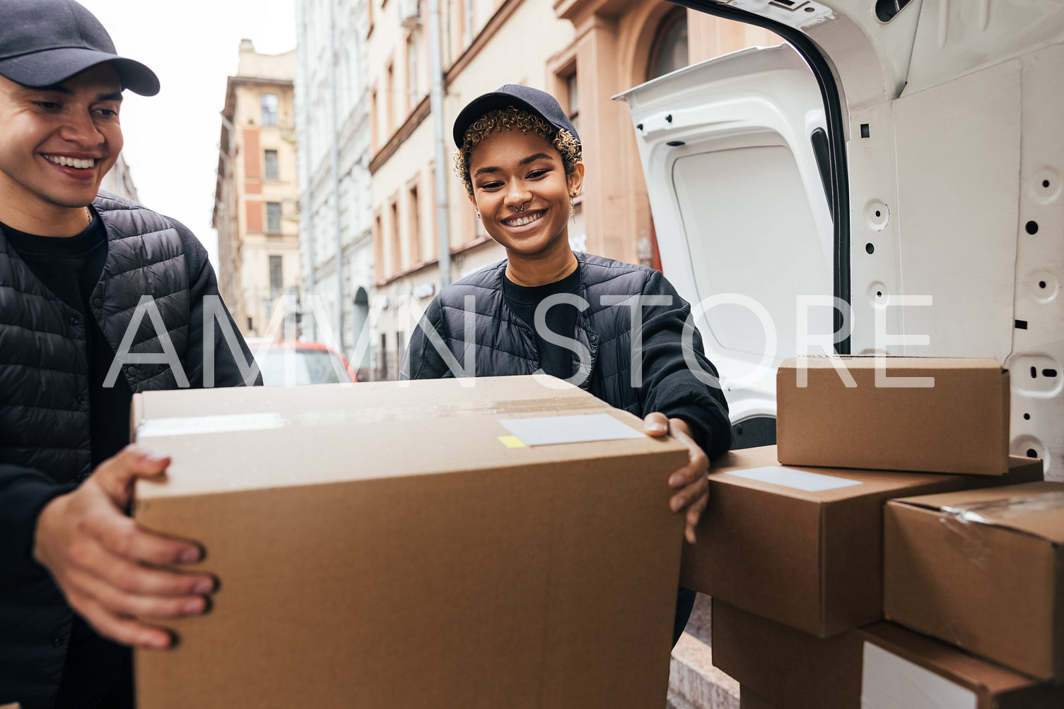 Two smiling coworkers unloading cardboard boxes from van for del