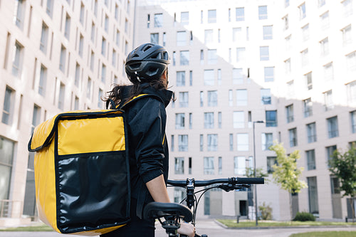 Rear view of a female courier with thermal backpack looking at an apartment building