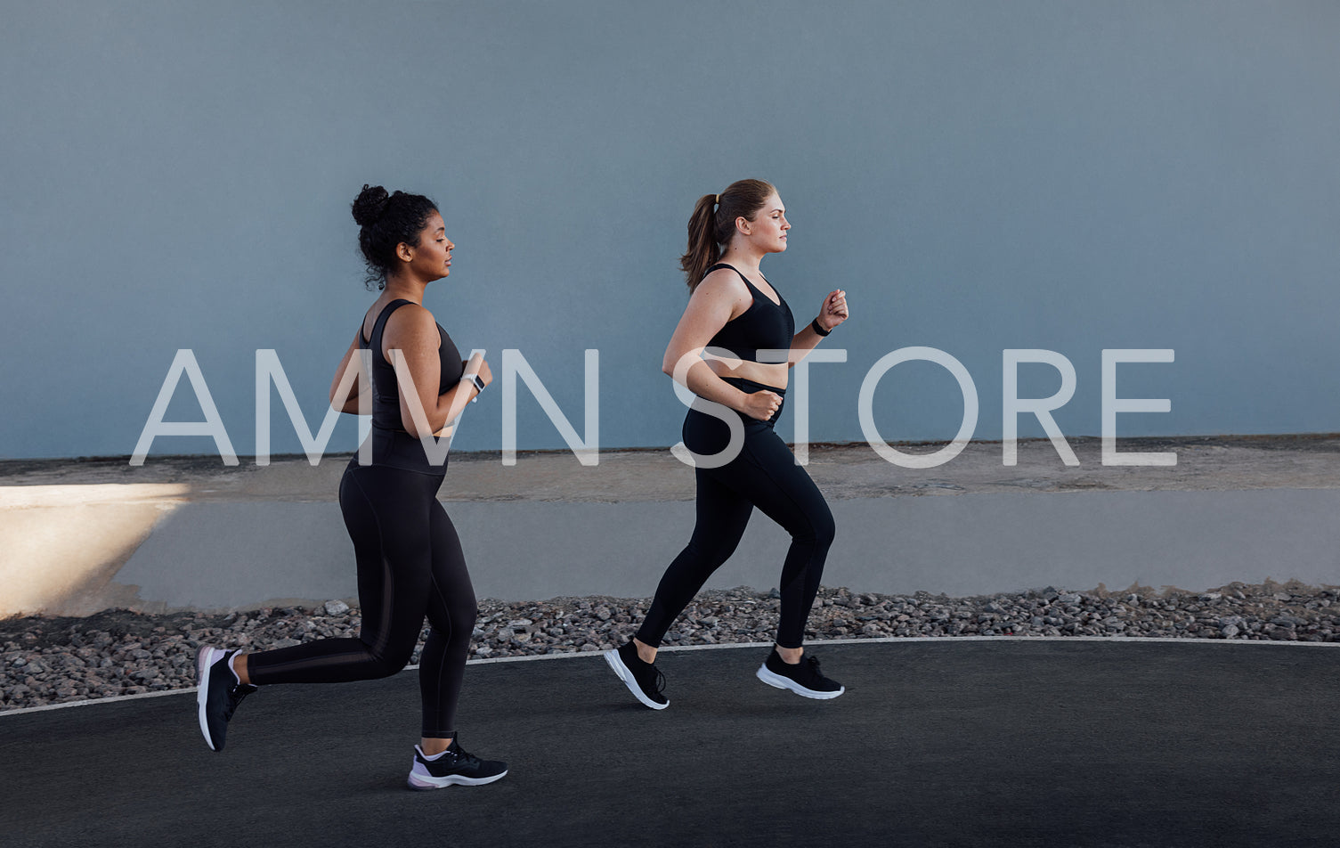 Two women with different body types running outdoors. Side view of two young females jogging at a grey wall.