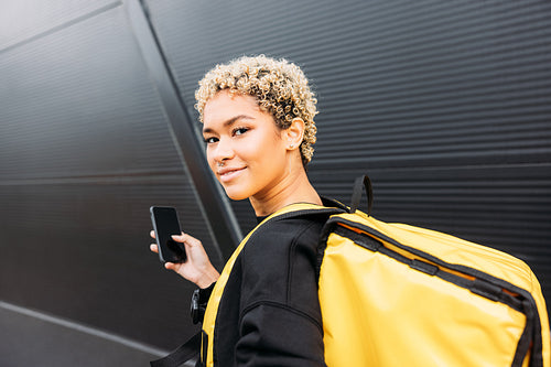 Portrait of smiling delivery woman with bag standing on a sidewa