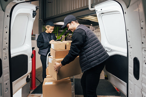 Side view male courier loads cardboard boxes from cart into the