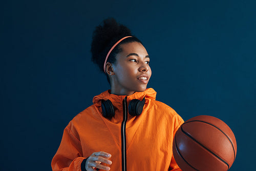 Portrait of a female professional basketball player looking away in a studio. Confident female basketball player wearing orange sportswear.