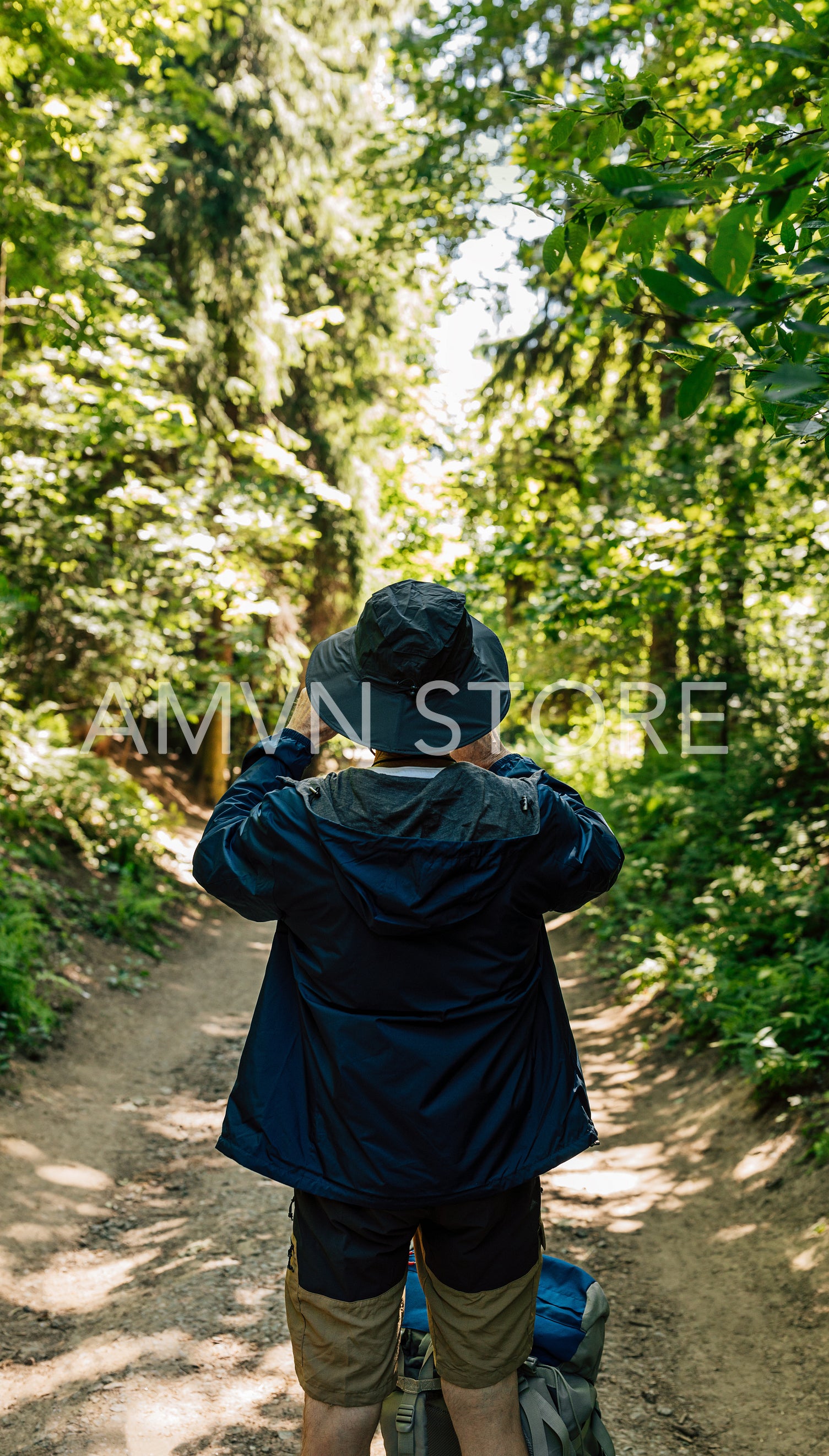 Back view of male in hat and hiking clothes taking photographs during trekking