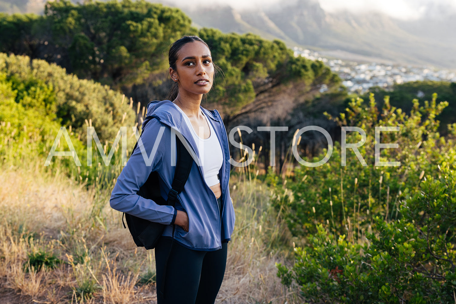 Confident sportswoman with backpack and sportswear standing in natural park 