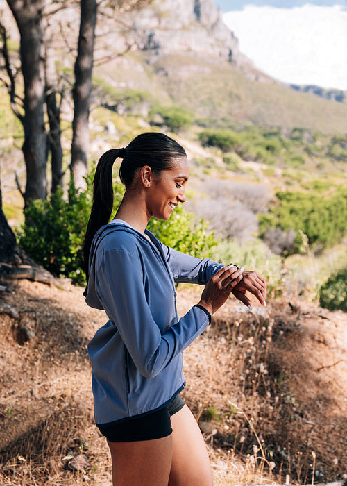 Side view of young and slim female in fitness wear checking her pulse on smartwatch