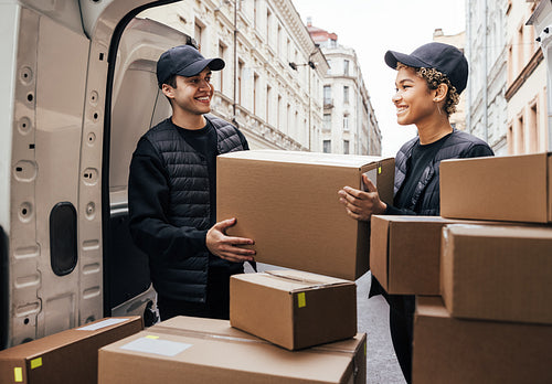 Two coworkers looking at each other while loads big cardboard box into a delivery van