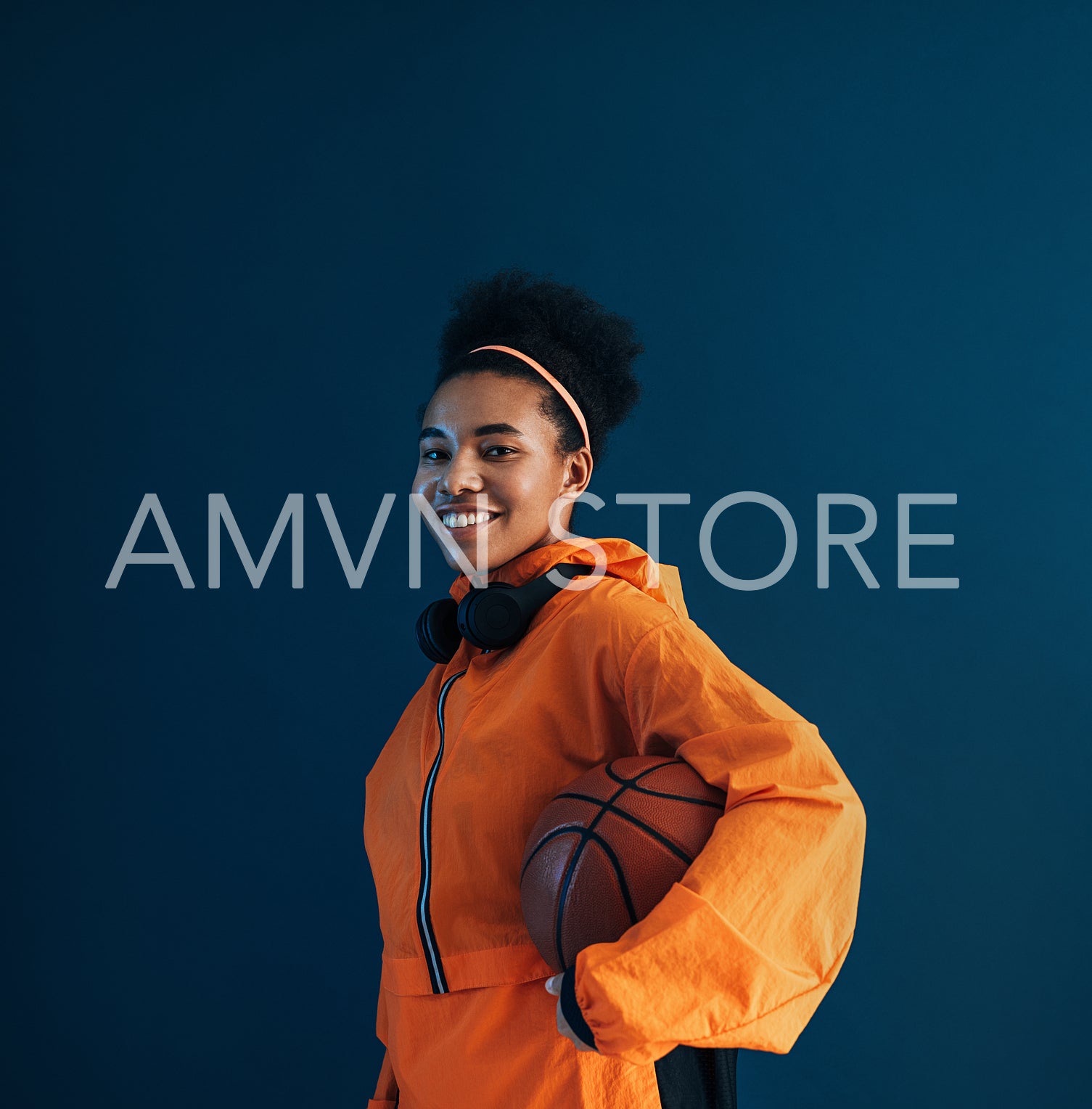 Professional basketball player in orange sportswear posing in studio against blue background