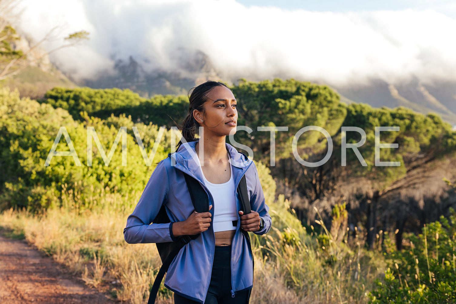 Young woman with backpack standing outdoors and watching sunset 