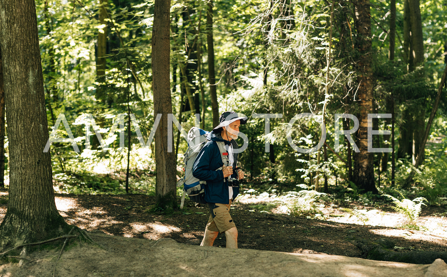 Side view of a senior male with a backpack and hiking clothes walking in the forest on sunny day