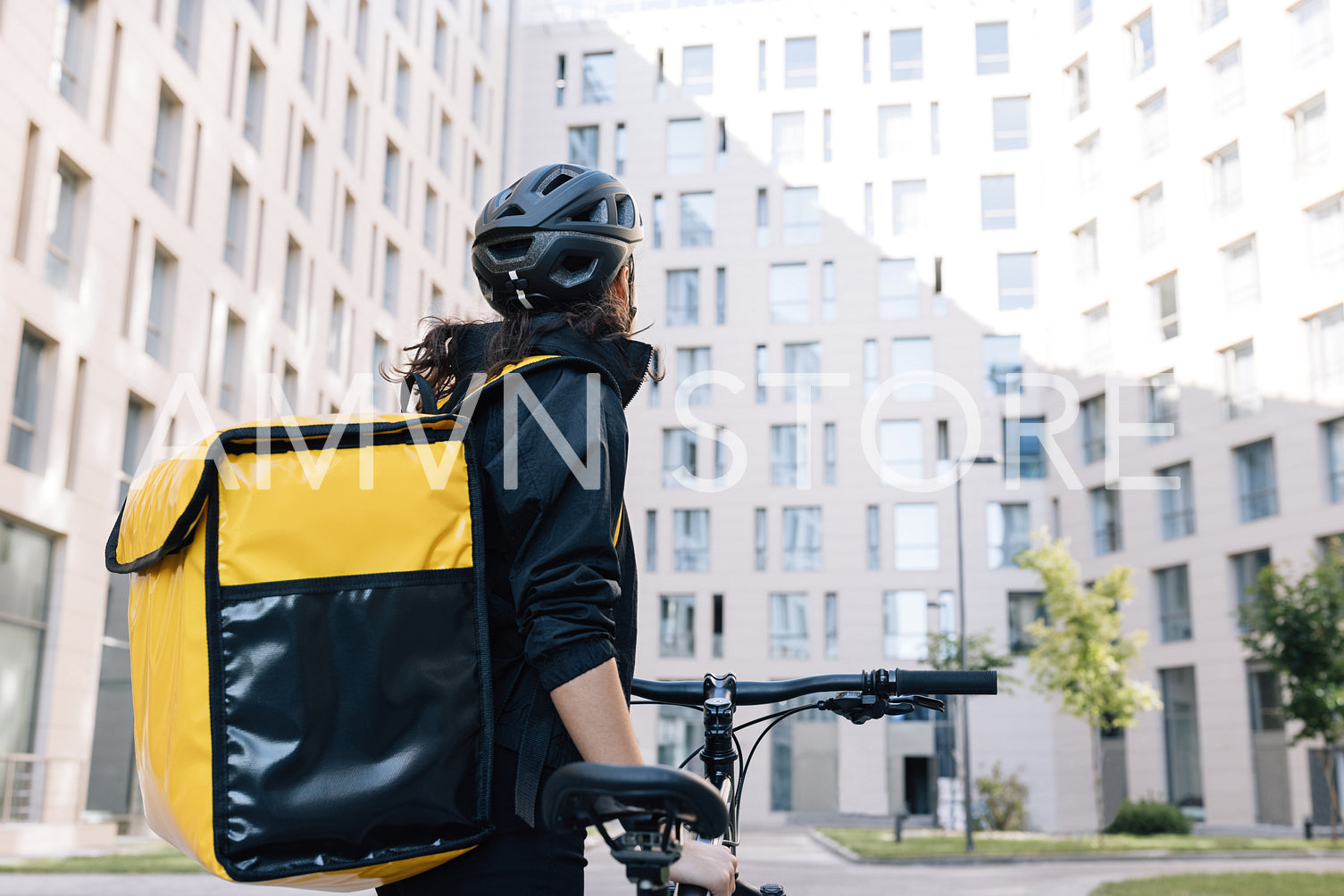 Rear view of a female courier with thermal backpack looking at an apartment building