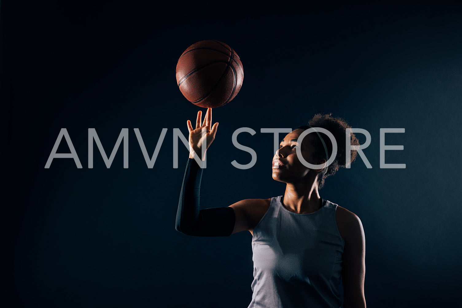 Studio shot of young sportswoman spins basketball on finger. Professional basketball player over black background.