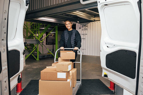 Smiling woman in uniform standing in warehouse with cart prepari