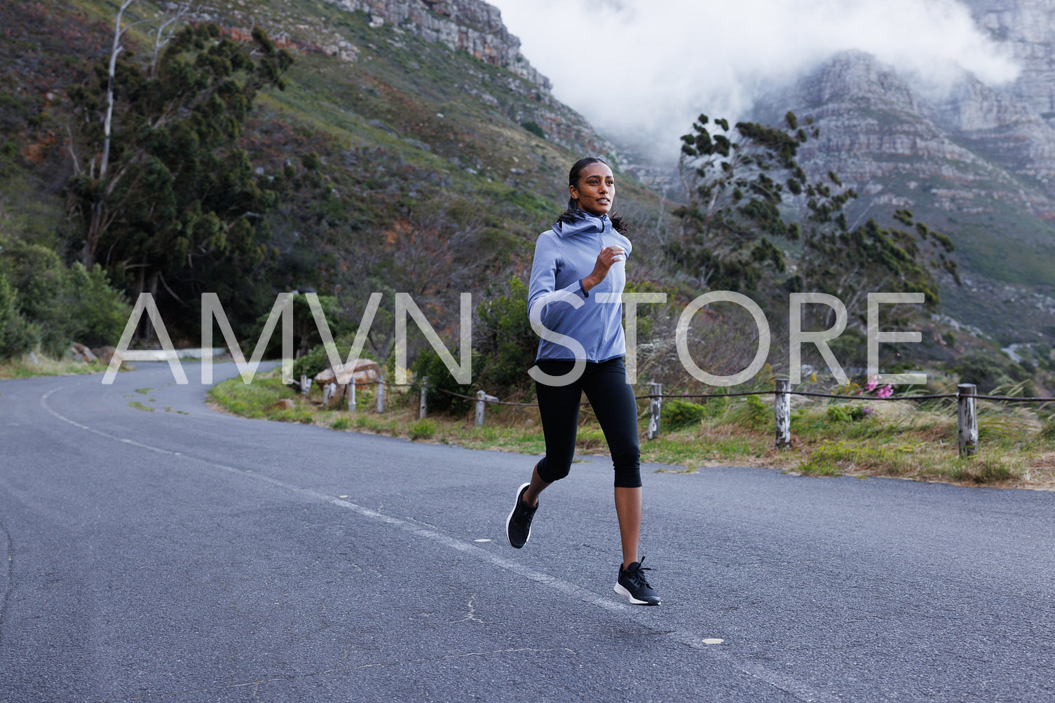 Full length of a slim female athlete running on an abandoned road. Woman in fitness attire jogging on the road in the mountains.