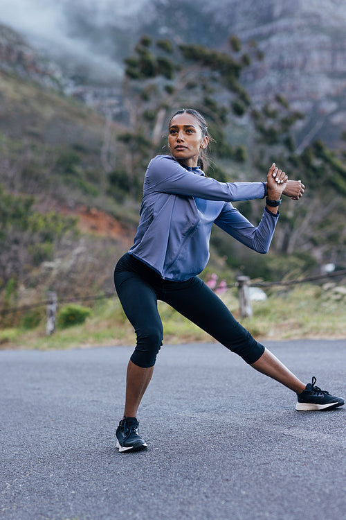 Confident female in sportswear warming up her body before outdoor run in natural park