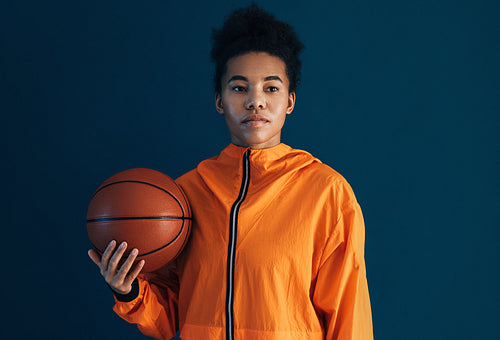 Portrait of a confident woman with basketball over blue backdrop looking away